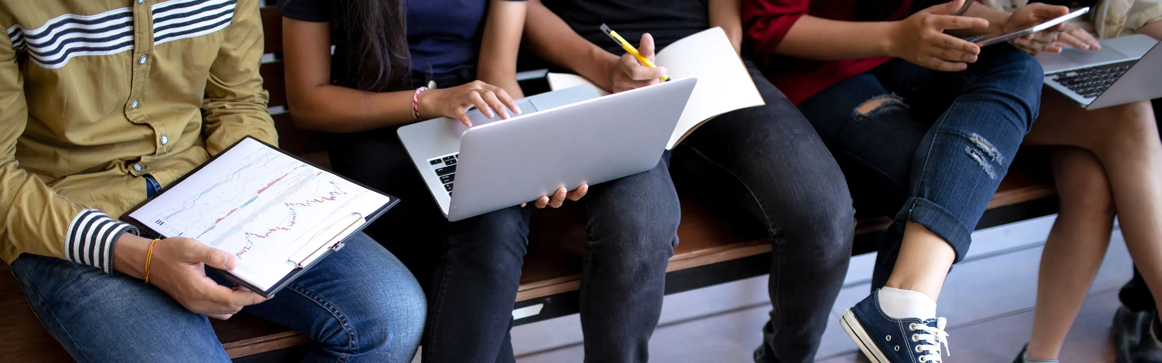 Gruppe junger Leute arbeitet gemeinsam mit Laptop, Tablet und Notizbuch.