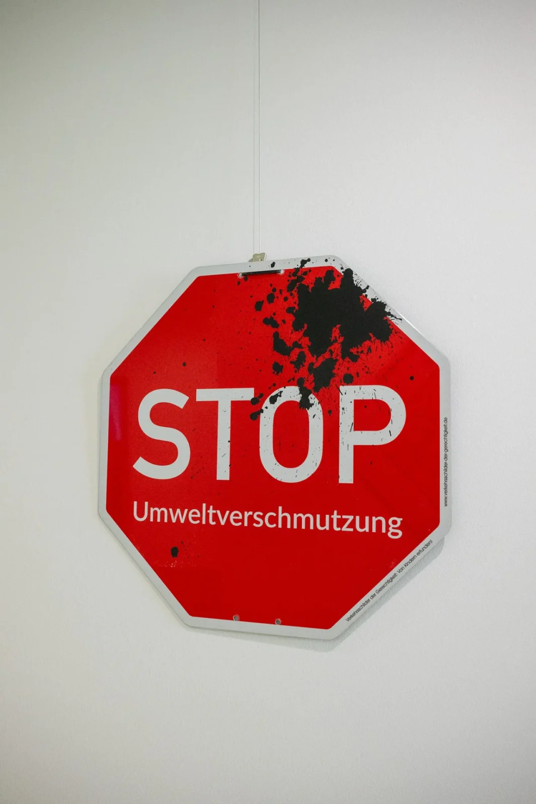 Kunst-Verkehrsschild „STOP Umweltverschmutzung" mit schwarzem Farbklecks an weißer Wand
