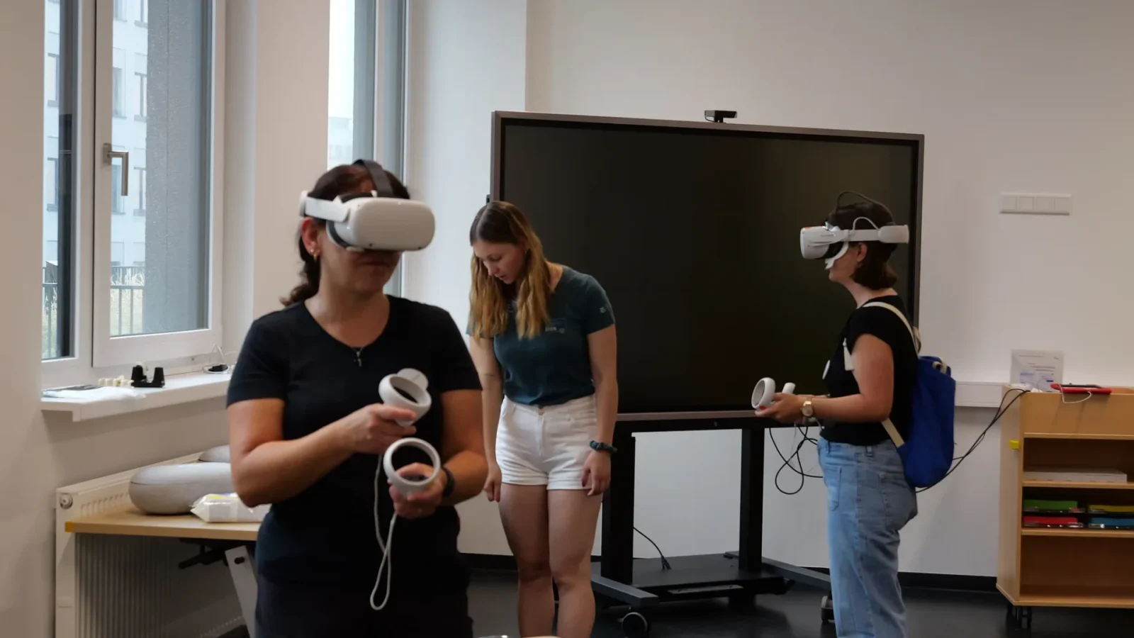 Zwei Teilnehmerinnen testen VR-Headsets und Controller vor einem großen Touchdisplay