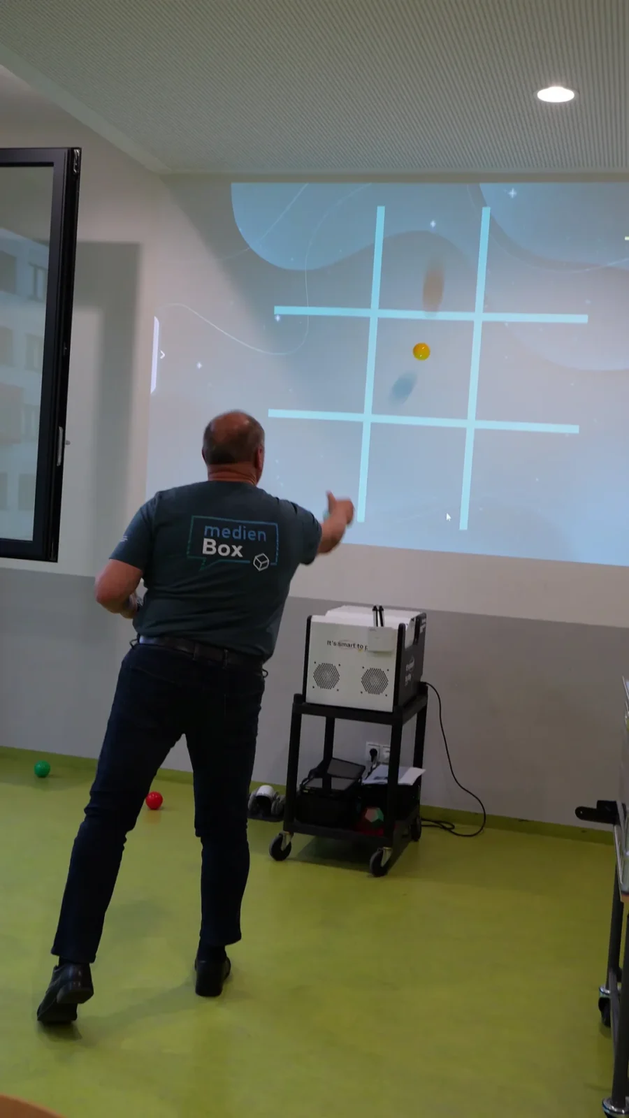Person wirft einen Ball auf ein interaktives Spielfeld, das an die Wand projiziert wird