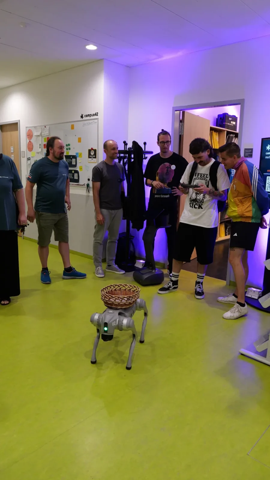 Roboterhund mit Weidenkorb auf dem Rücken läuft durch den Flur, Gäste steuern ihn per Tablet