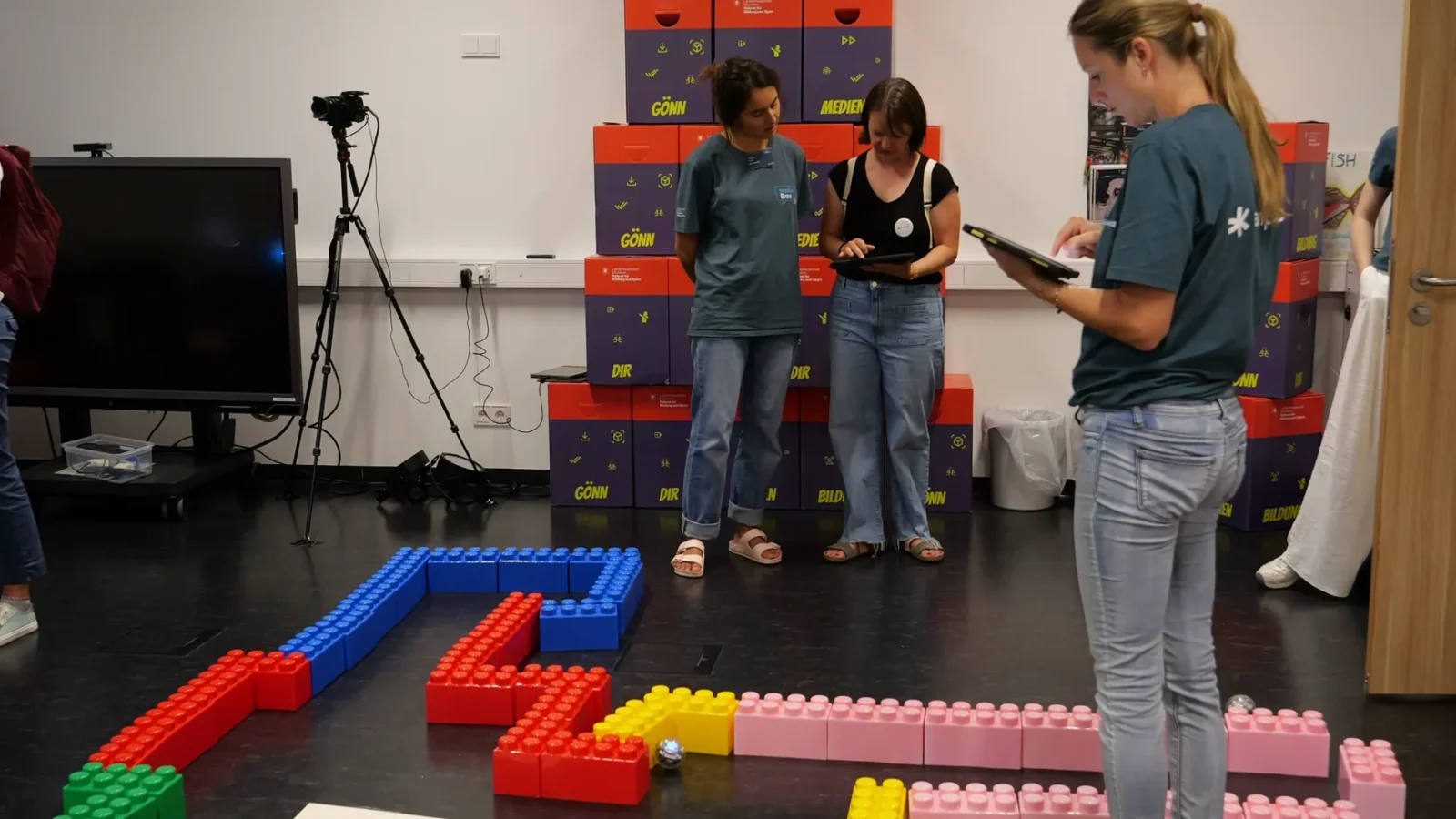 Team an Tablets steuert einen Lernroboter durch einen Parcours aus großen Bausteinen
