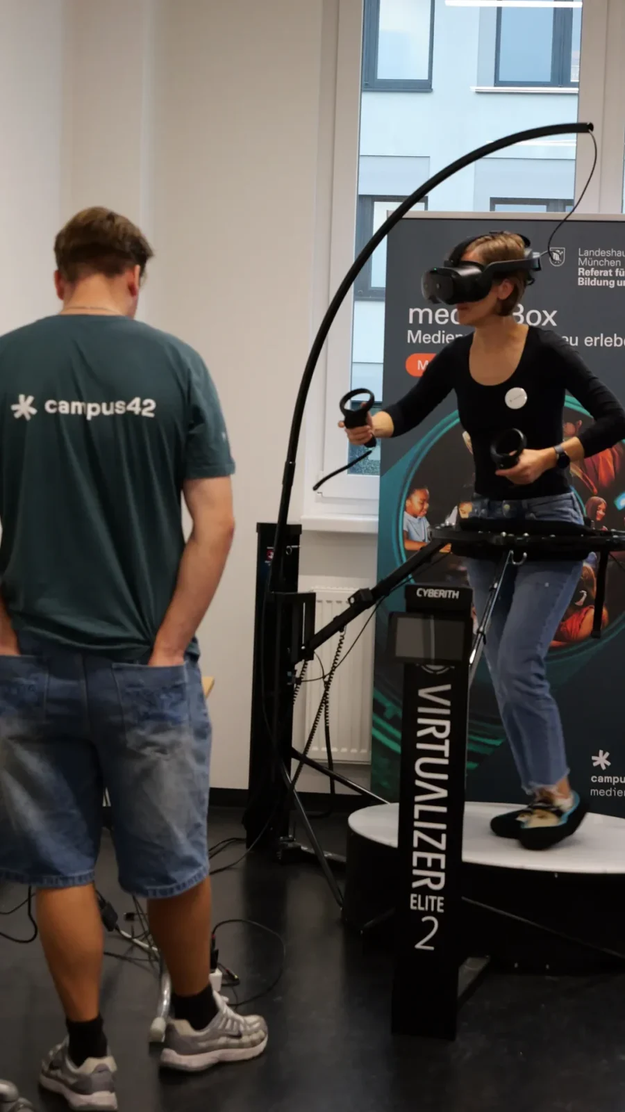 Person mit VR-Brille läuft auf einer Cyberith-Virtualizer-Laufplattform, Betreuer daneben