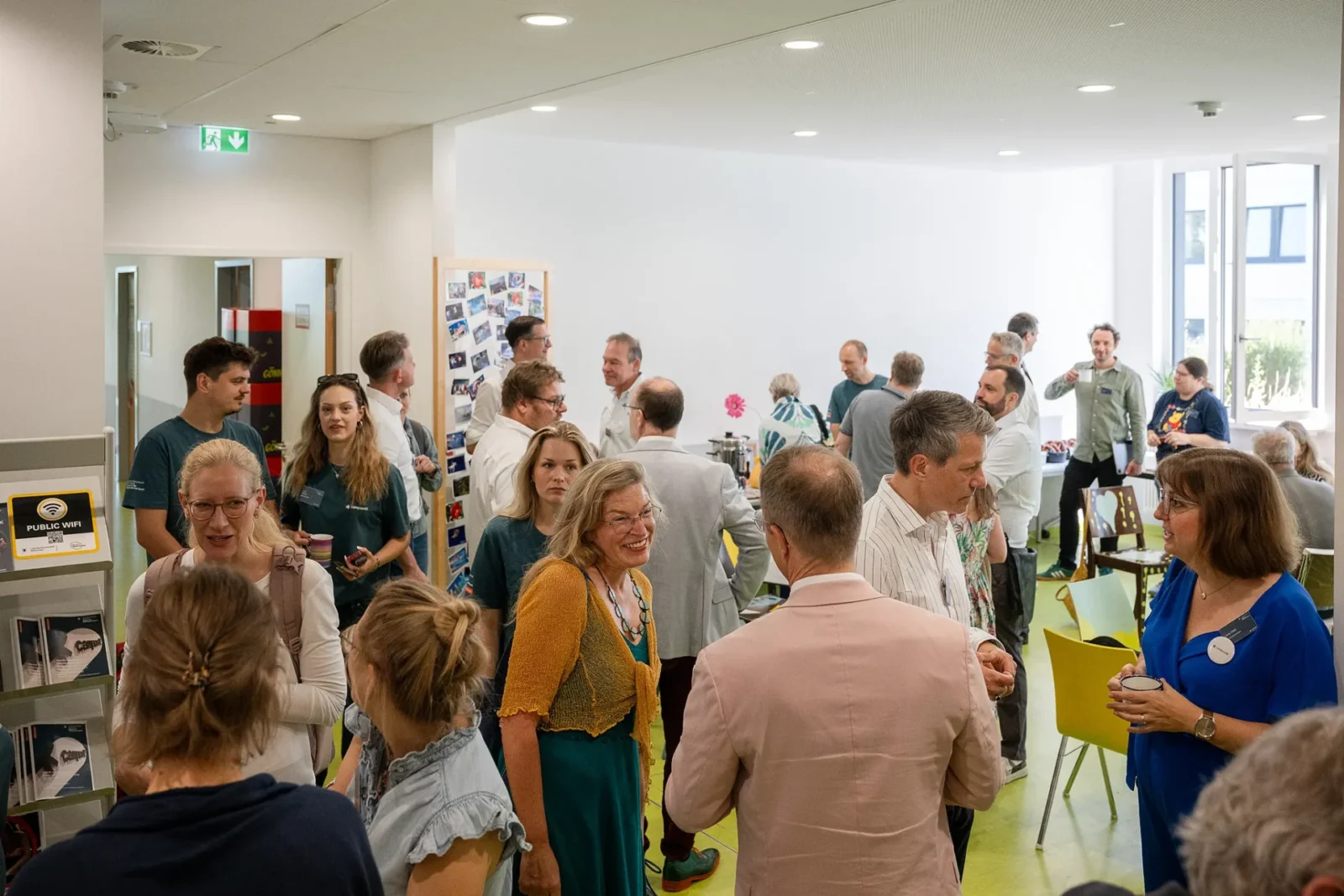 Volles Foyer beim Sommerempfang: Gäste mit Tassen im Gespräch, Team in campus42-Shirts, Fotowand und Kaffeetheke