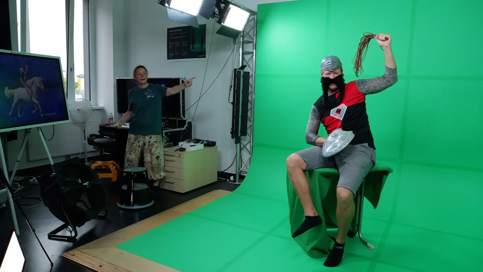 Als Ritter verkleideter Mann posiert im Greenscreen-Studio, Monitor zeigt ihn auf einem Einhorn