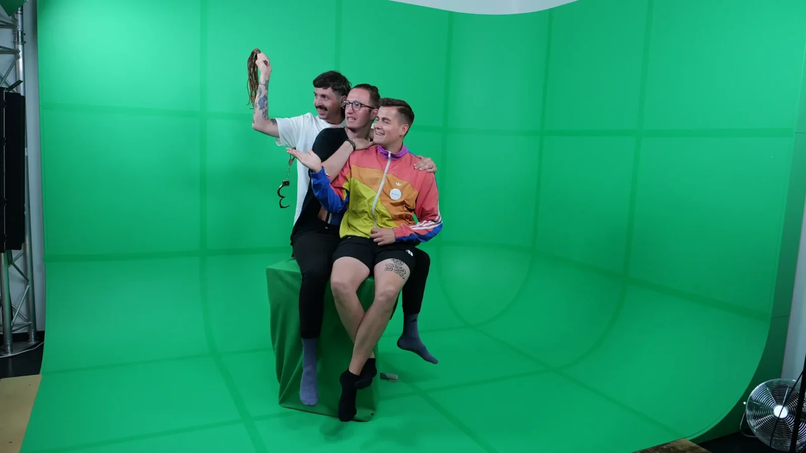 Drei Personen sitzen auf einem grünen Würfel vor der Greenscreen-Hohlkehle und posieren