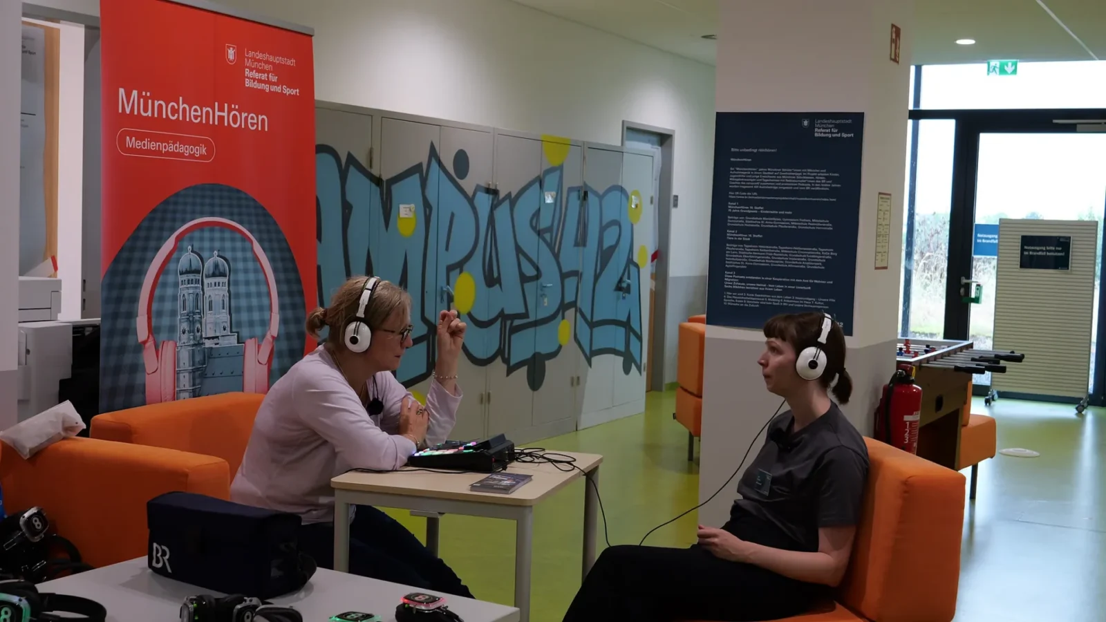 Zwei Frauen mit Kopfhörern beim Podcast-Interview am Mischpult vor MünchenHören-Rollup