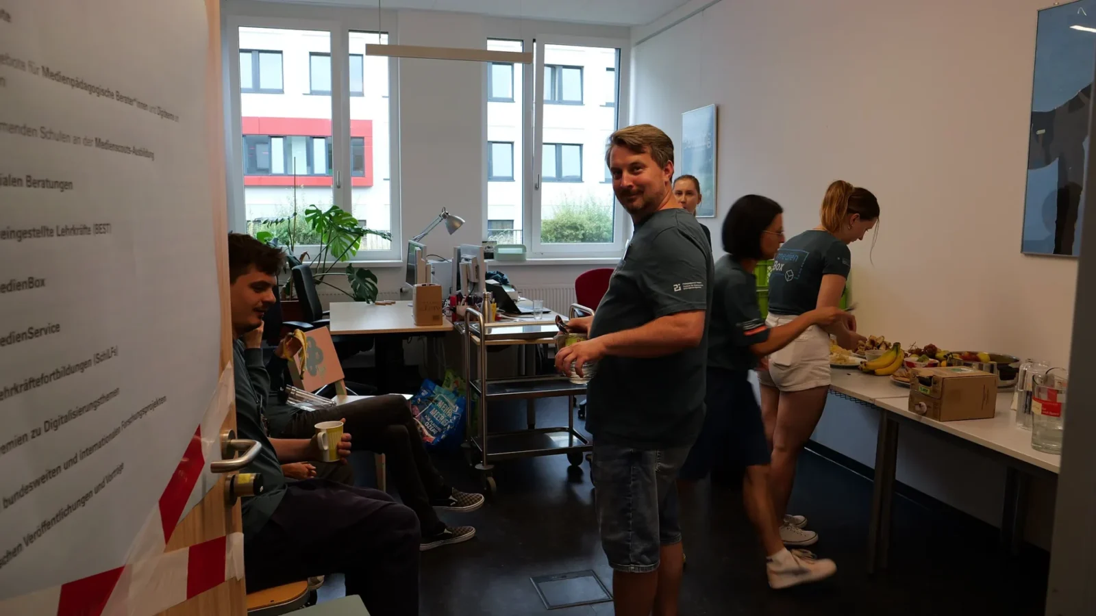 Team am Buffet mit Obst, links Flipchart mit den Angeboten medienBox, medienService und SchiLFs