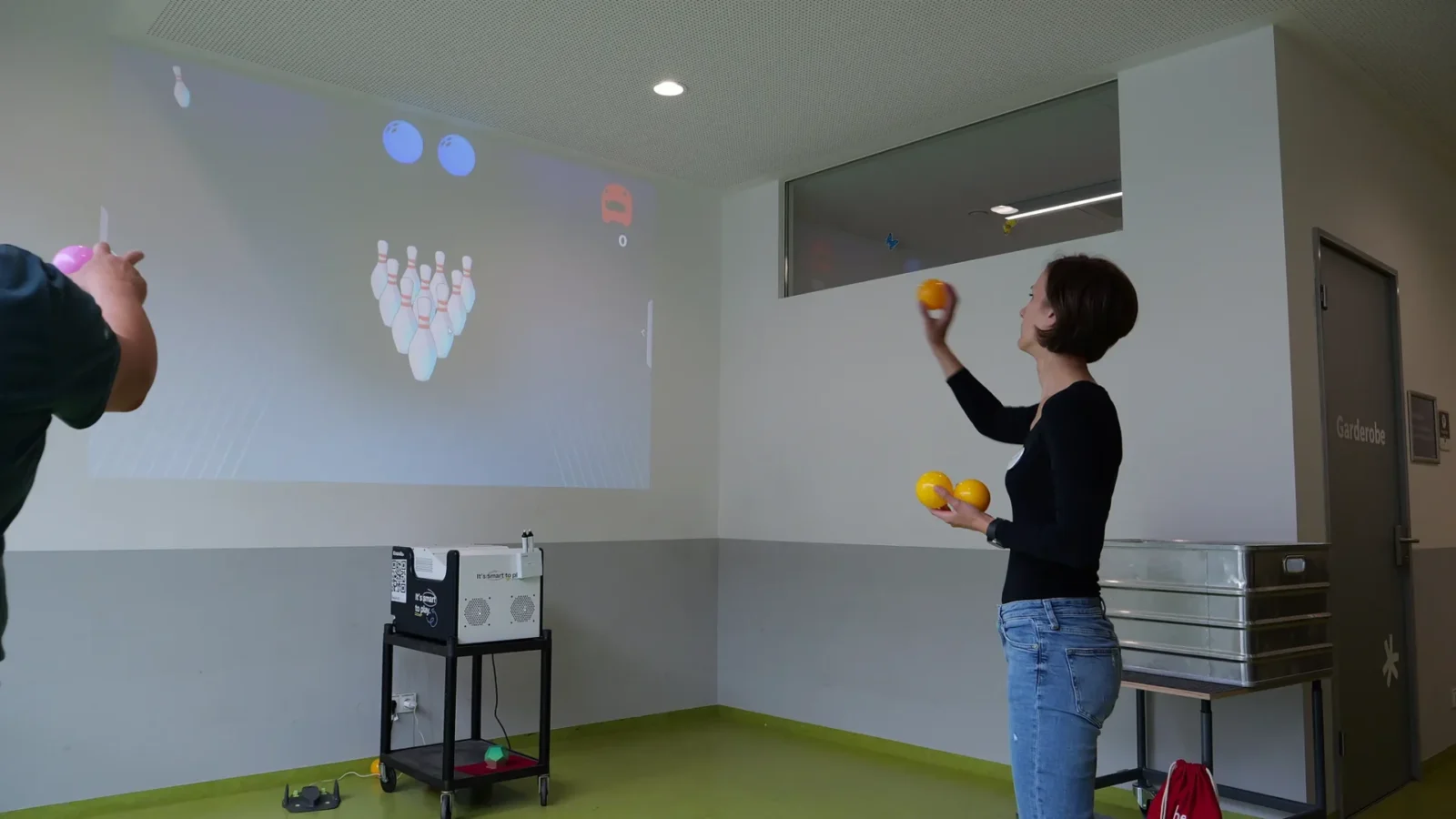 Frau jongliert mit drei Bällen vor einer interaktiven Bowling-Projektion