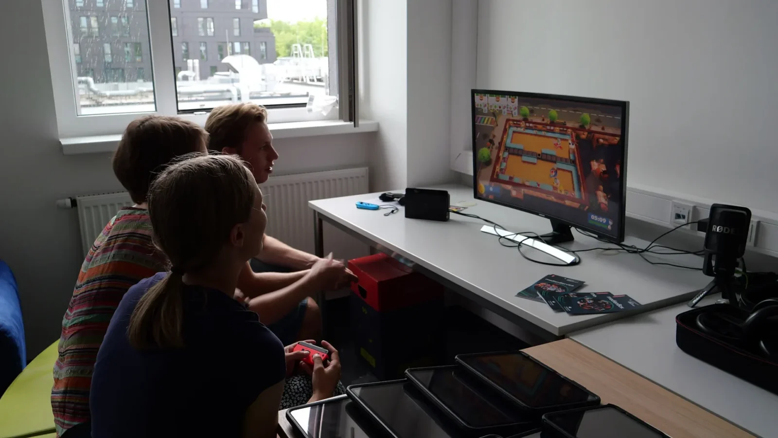 Drei Personen spielen mit Switch-Controllern ein Koch-Videospiel im Gaming-Bereich