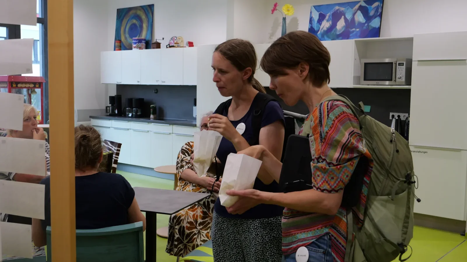 Zwei Besucherinnen mit Popcorntüten im Cafébereich, im Hintergrund die Popcornmaschine