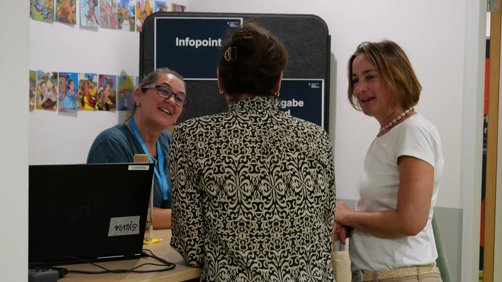 Beratungsgespräch am Tresen mit Schild „Infopoint", eine Mitarbeiterin am Laptop