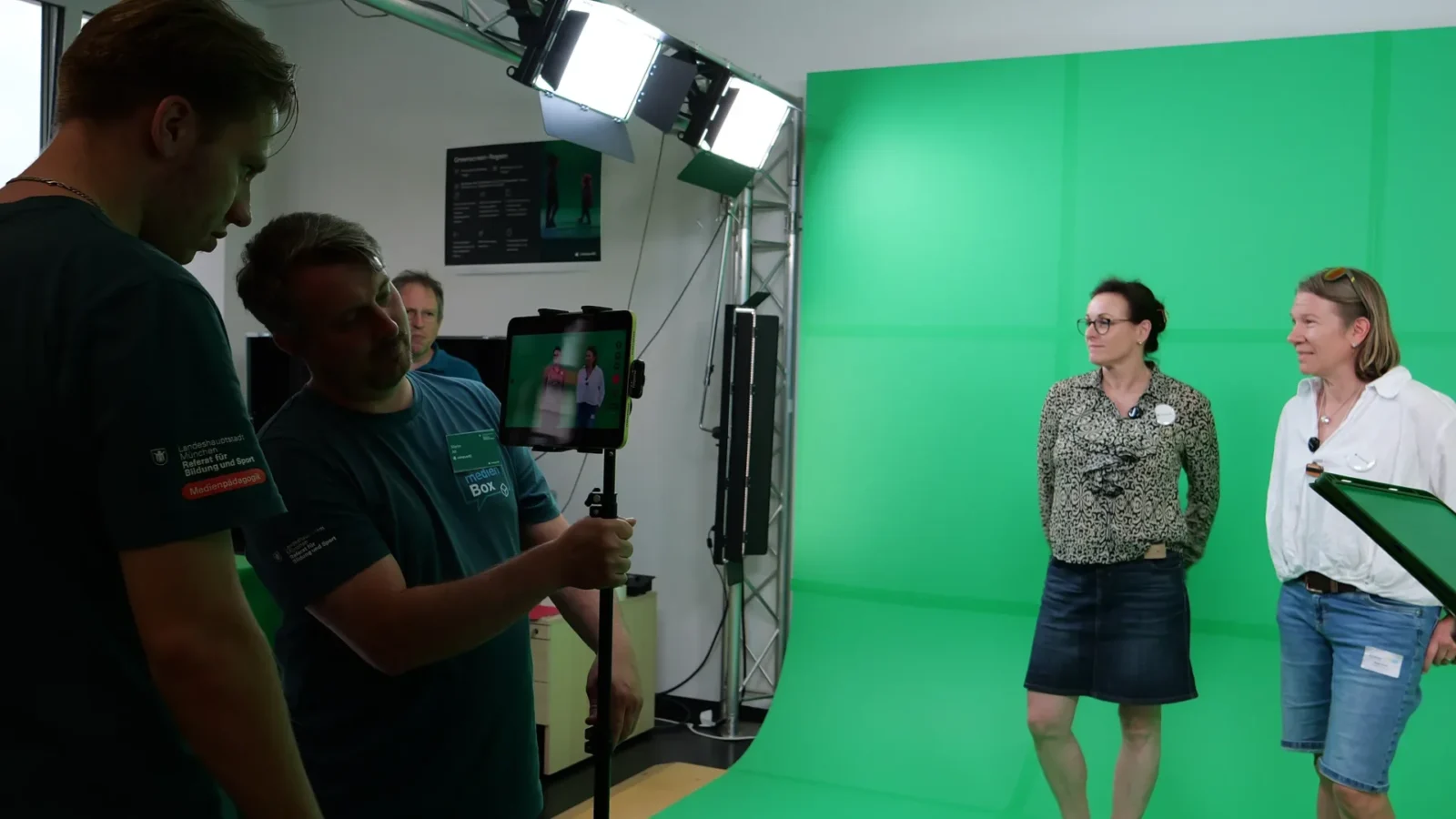 Mitarbeiter filmt mit Tablet auf Stativ zwei Besucherinnen vor der grünen Greenscreen-Wand