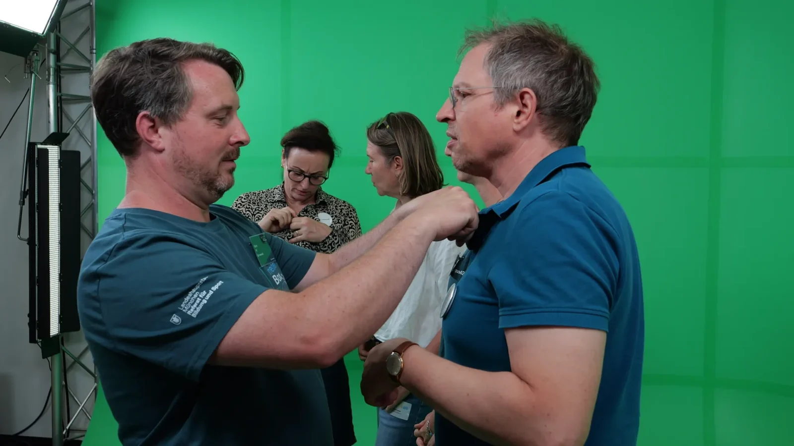 Ansteckmikrofon wird einem Besucher befestigt, weitere Gäste verkabeln sich vor dem Greenscreen