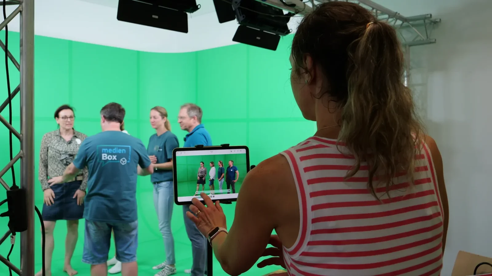 Blick auf ein Tablet, das die Gruppe vor der Greenscreen-Wand als Livebild zeigt