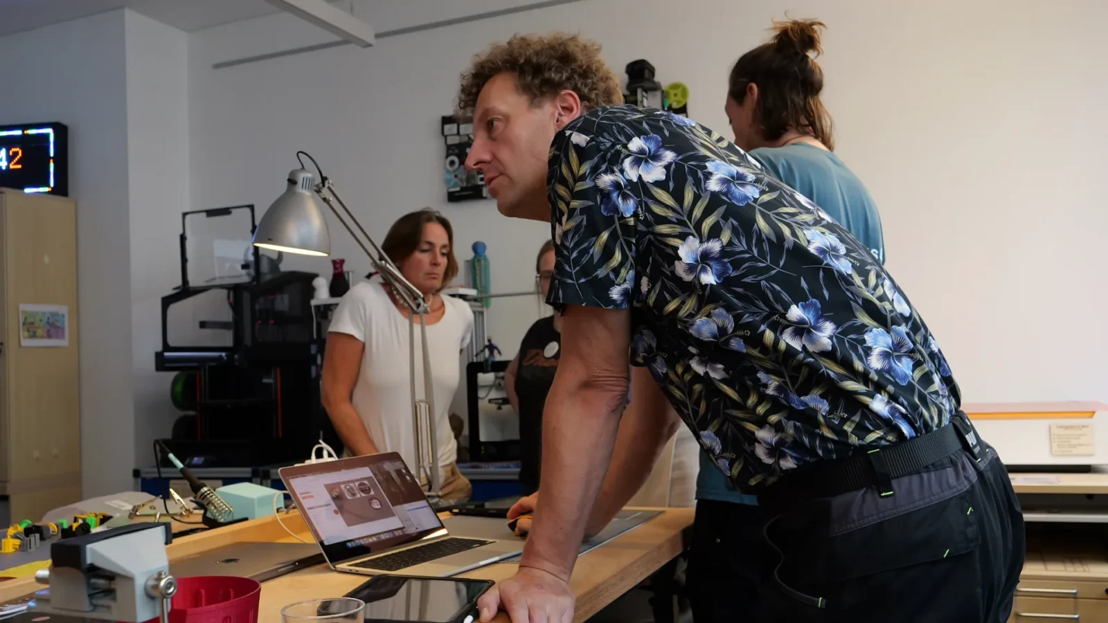Person arbeitet an einem Laptop im Makerspace, im Hintergrund 3D-Drucker und Lötstation