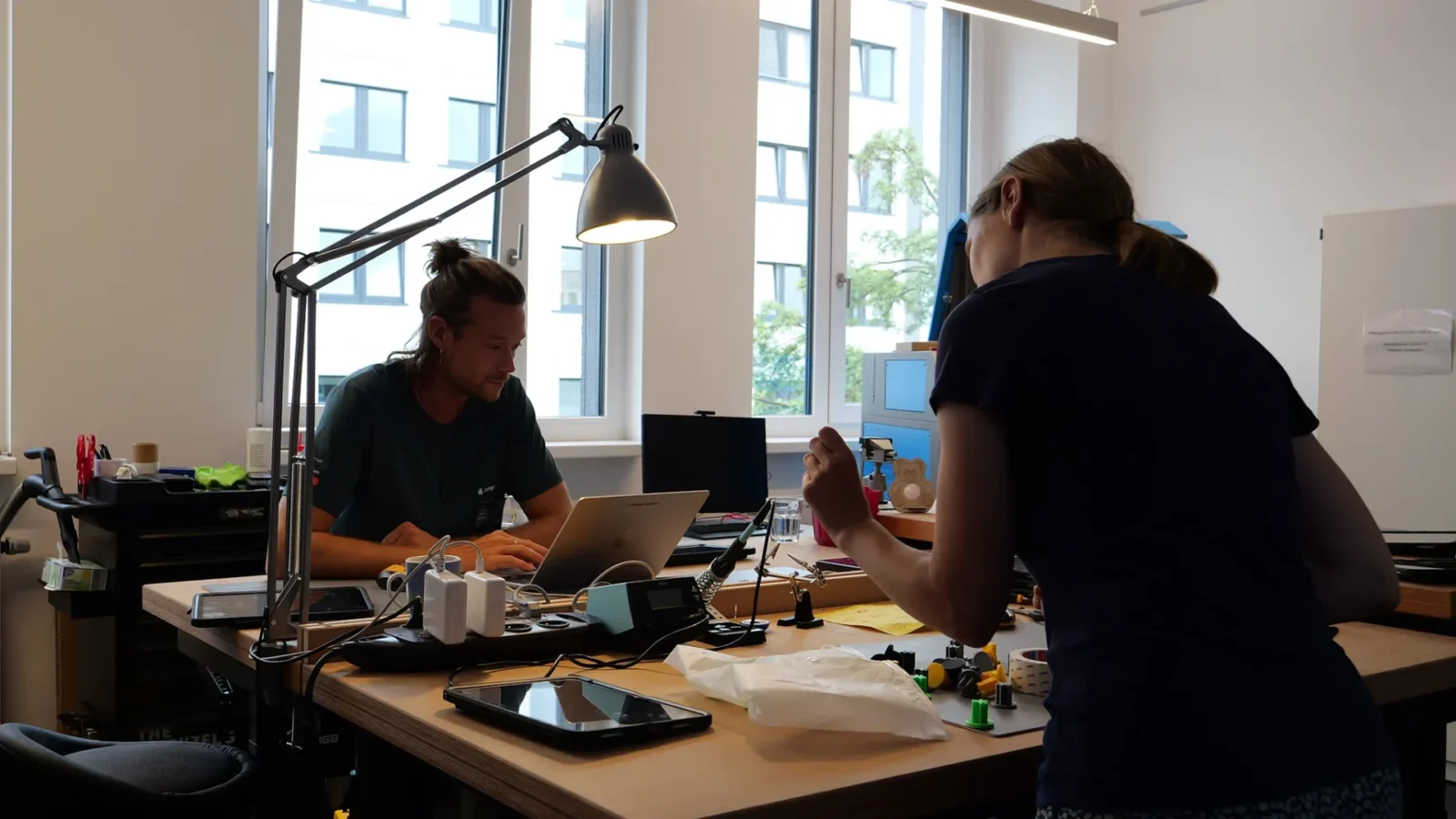 Werkbank im Makerspace mit Lötstation, Tablets und 3D-Druckteilen