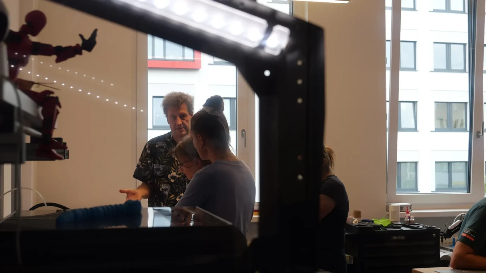 Blick durch einen 3D-Drucker auf eine Besuchergruppe im Makerspace