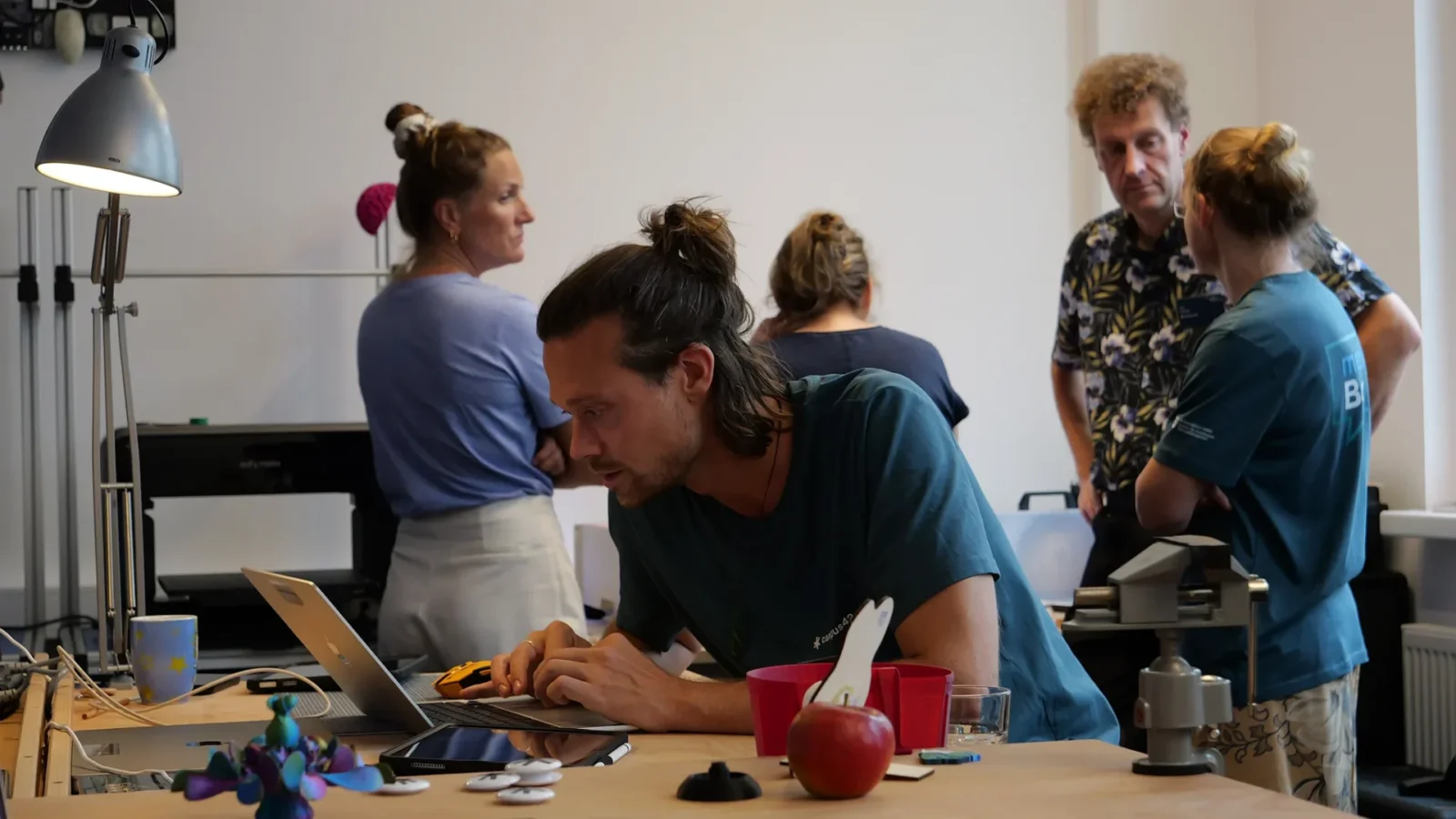 Person tippt am Laptop im Makerspace, im Vordergrund 3D-gedruckte Objekte und Buttons