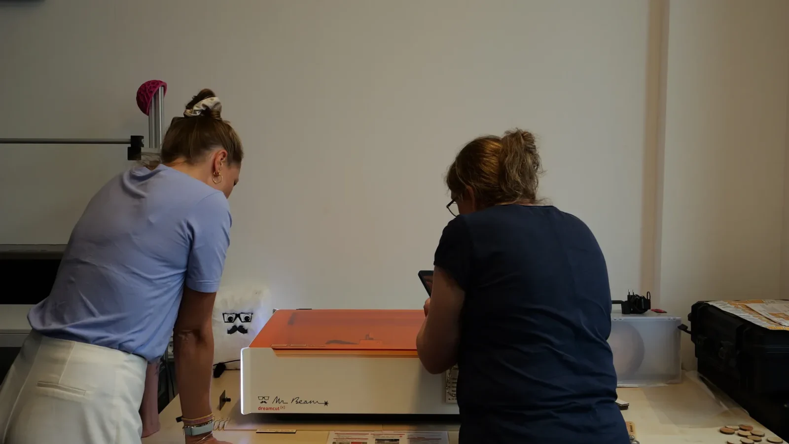 Zwei Personen bedienen einen Mr-Beam-Lasercutter, daneben lasergeschnittene Holzscheiben