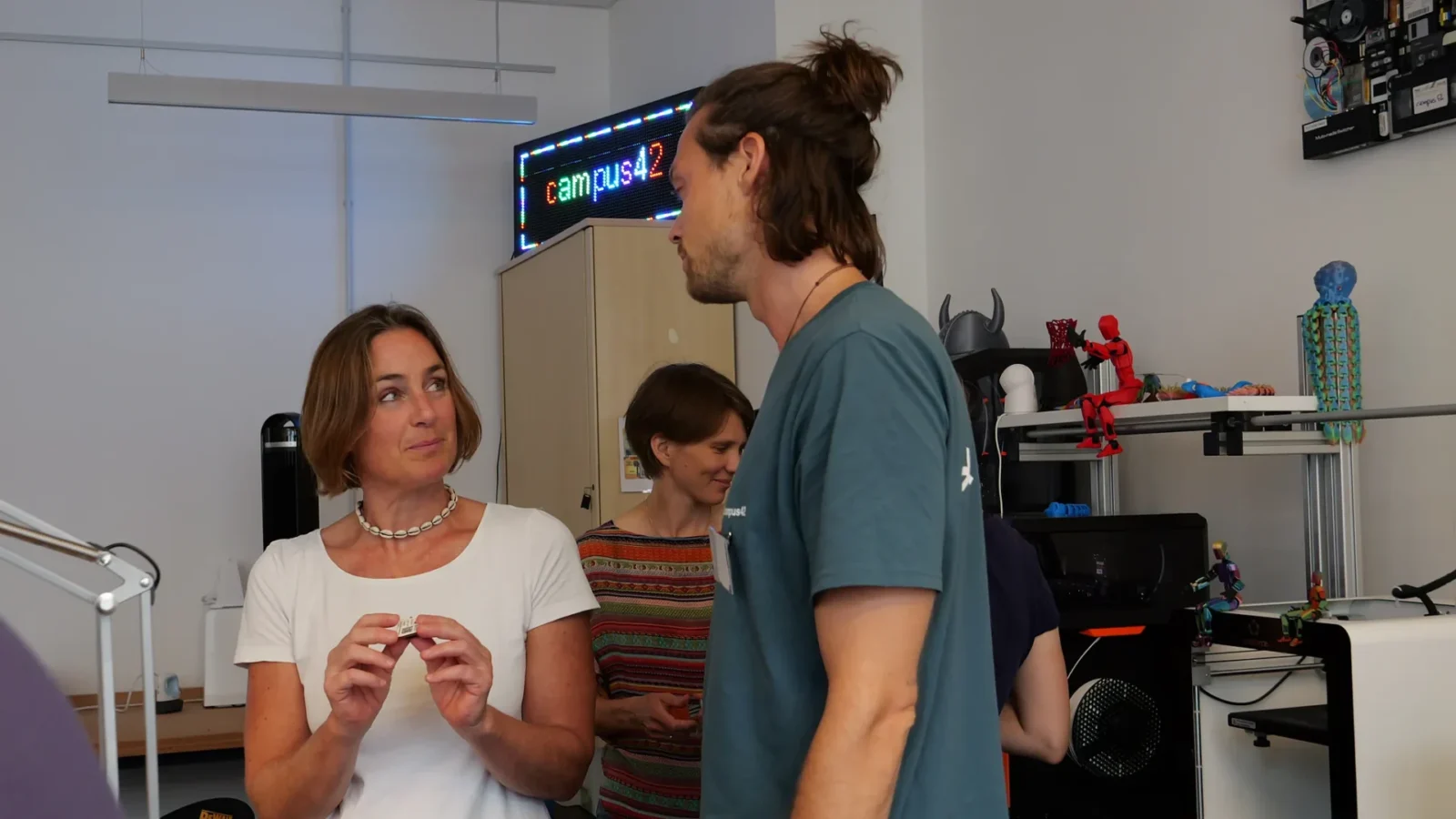 Gespräch im Makerspace, im Hintergrund leuchtender LED-Schriftzug campus42