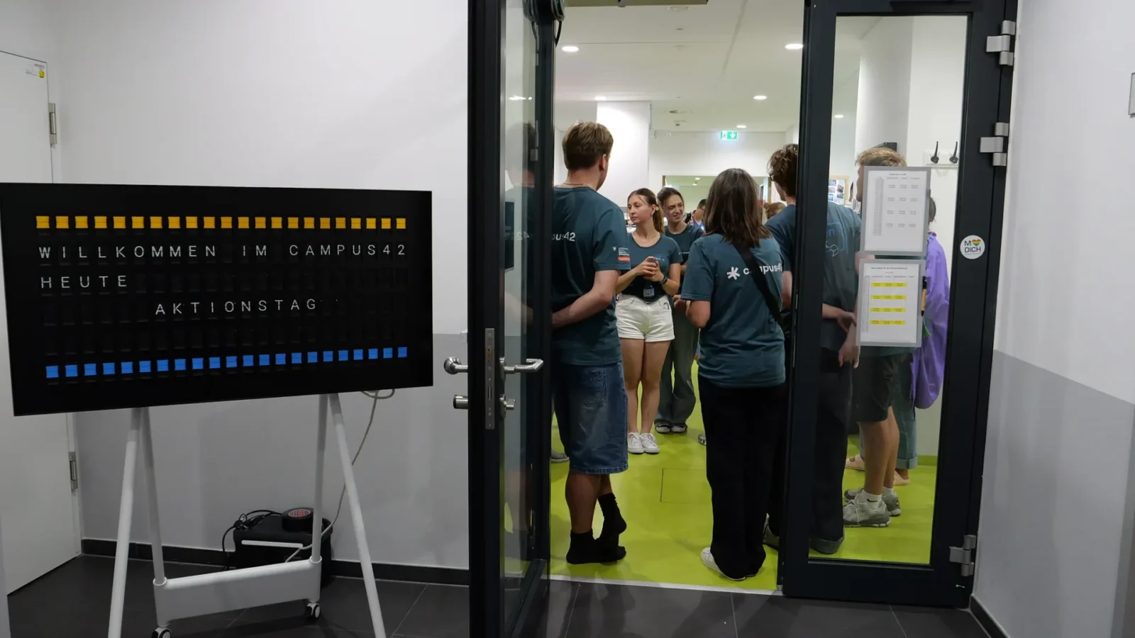 Fallblattanzeige „Willkommen im campus42 – Heute Aktionstag", dahinter das Team im Eingangsbereich