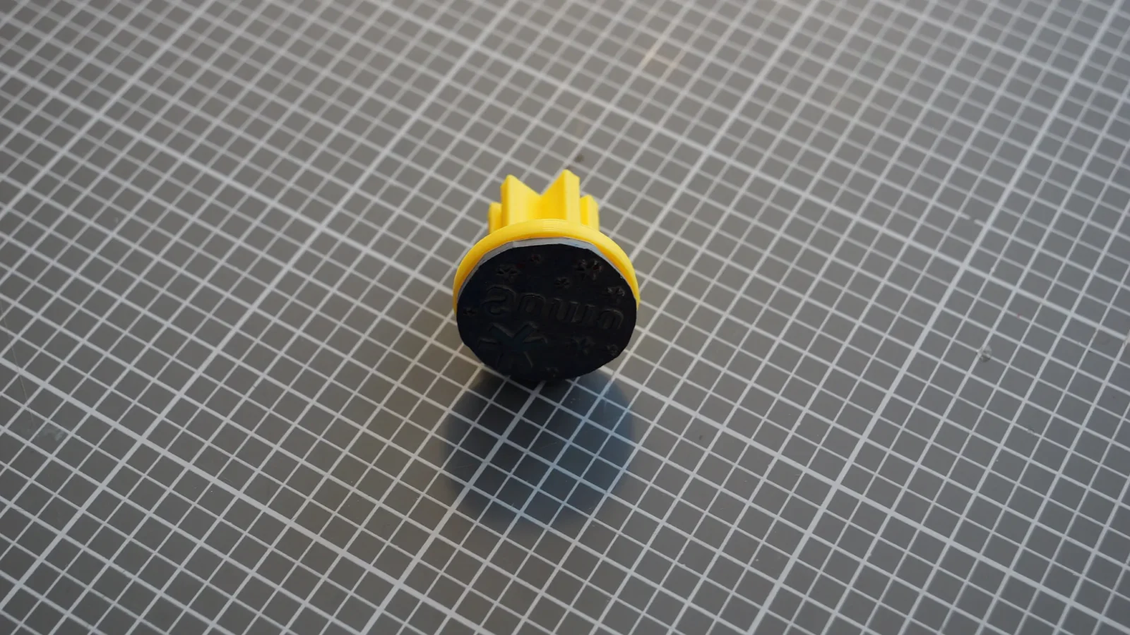 Gelb-schwarzer 3D-gedruckter Stempel mit campus42-Logo auf einer Schneidematte