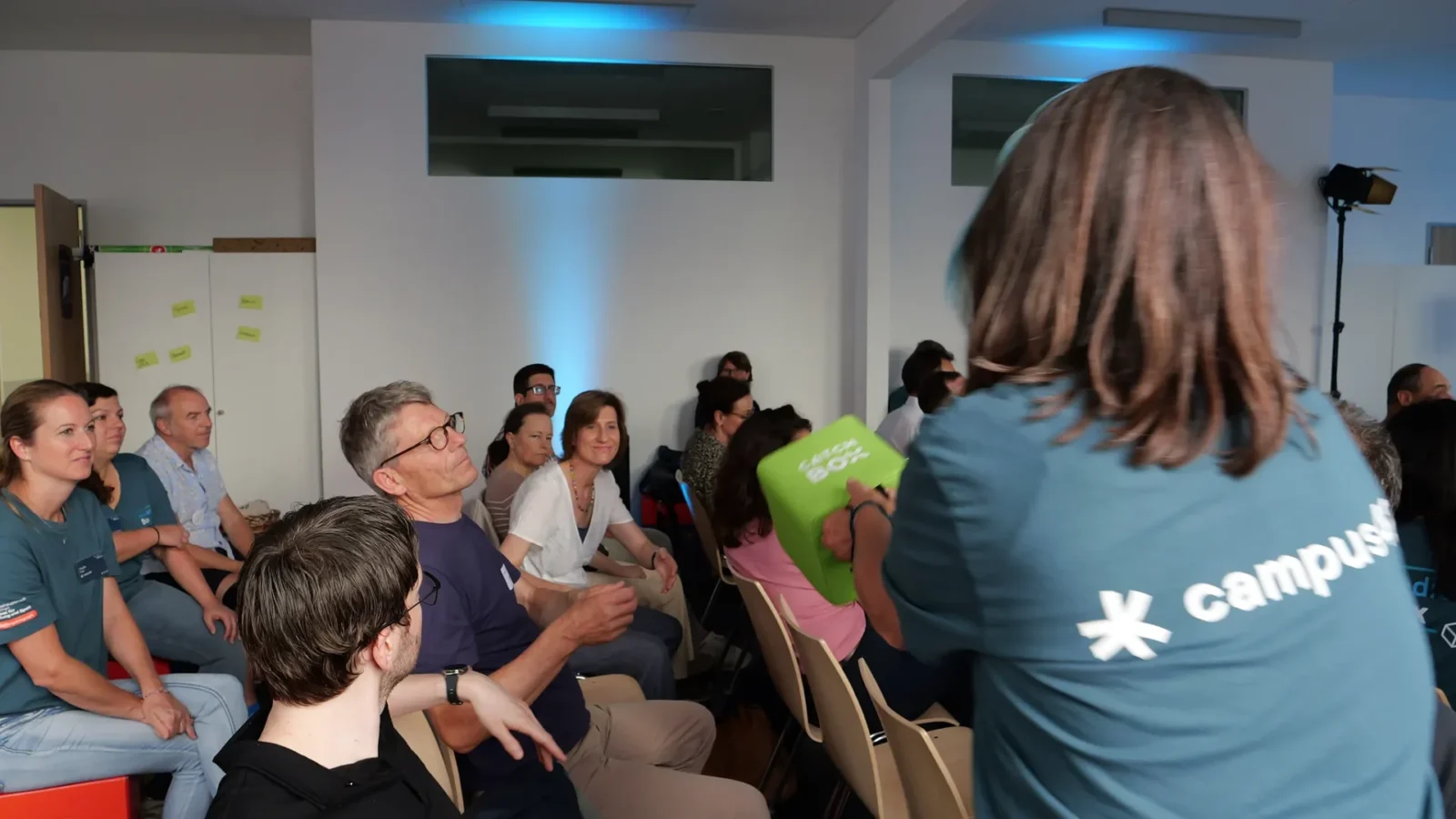 Person im campus42-Shirt wirft einen grünen Catchbox-Wurfwürfel ins sitzende Publikum