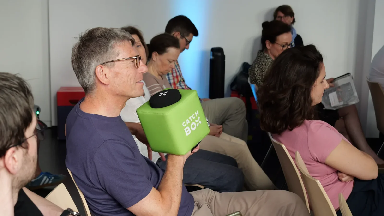 Publikumsfrage mit grünem Catchbox-Wurfmikrofon in der Stuhlreihe während eines Vortrags