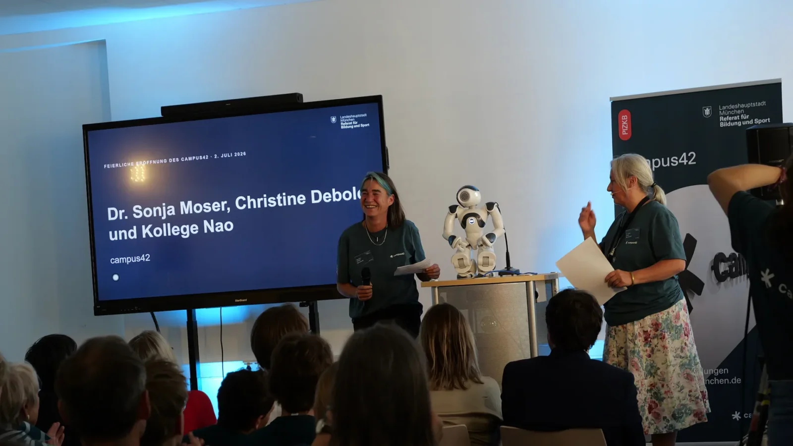 Moderatorin mit Mikrofon neben dem humanoiden Roboter Nao auf dem Pult