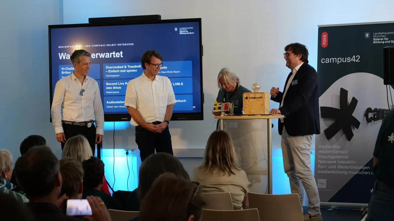 Vier Personen auf der Bühne vor der Folie „Medienparcours – den campus42 selbst entdecken"
