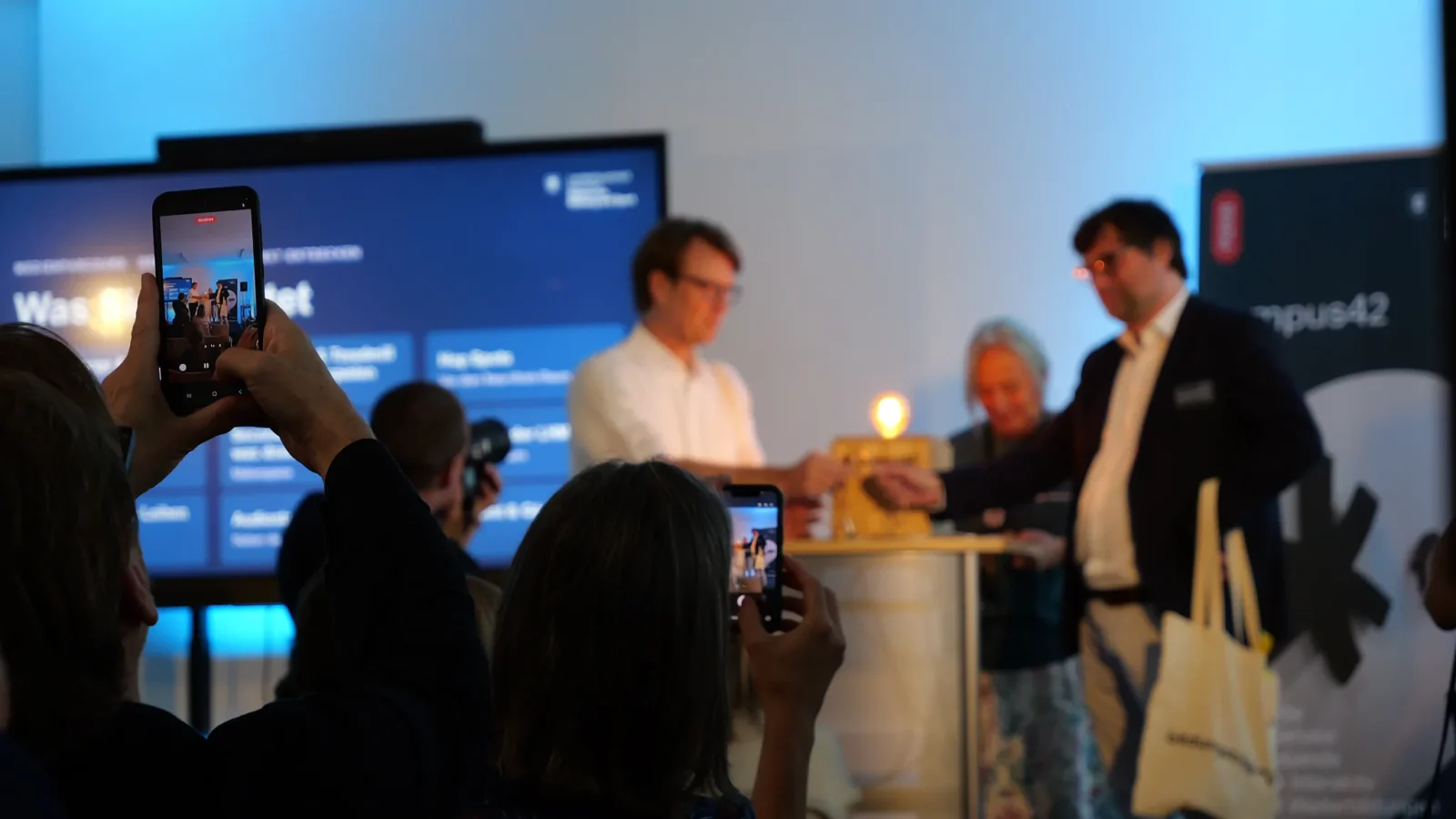 Zuschauende filmen mit Smartphones die Bühnenszene mit der leuchtenden campus42-Box