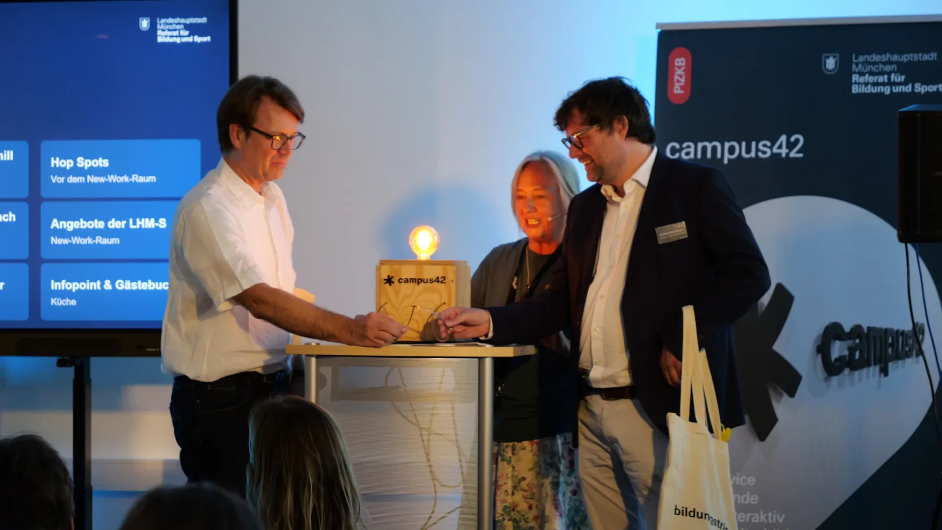 Drei Personen betätigen gemeinsam den Schalter der campus42-Holzbox, die Glühbirne leuchtet