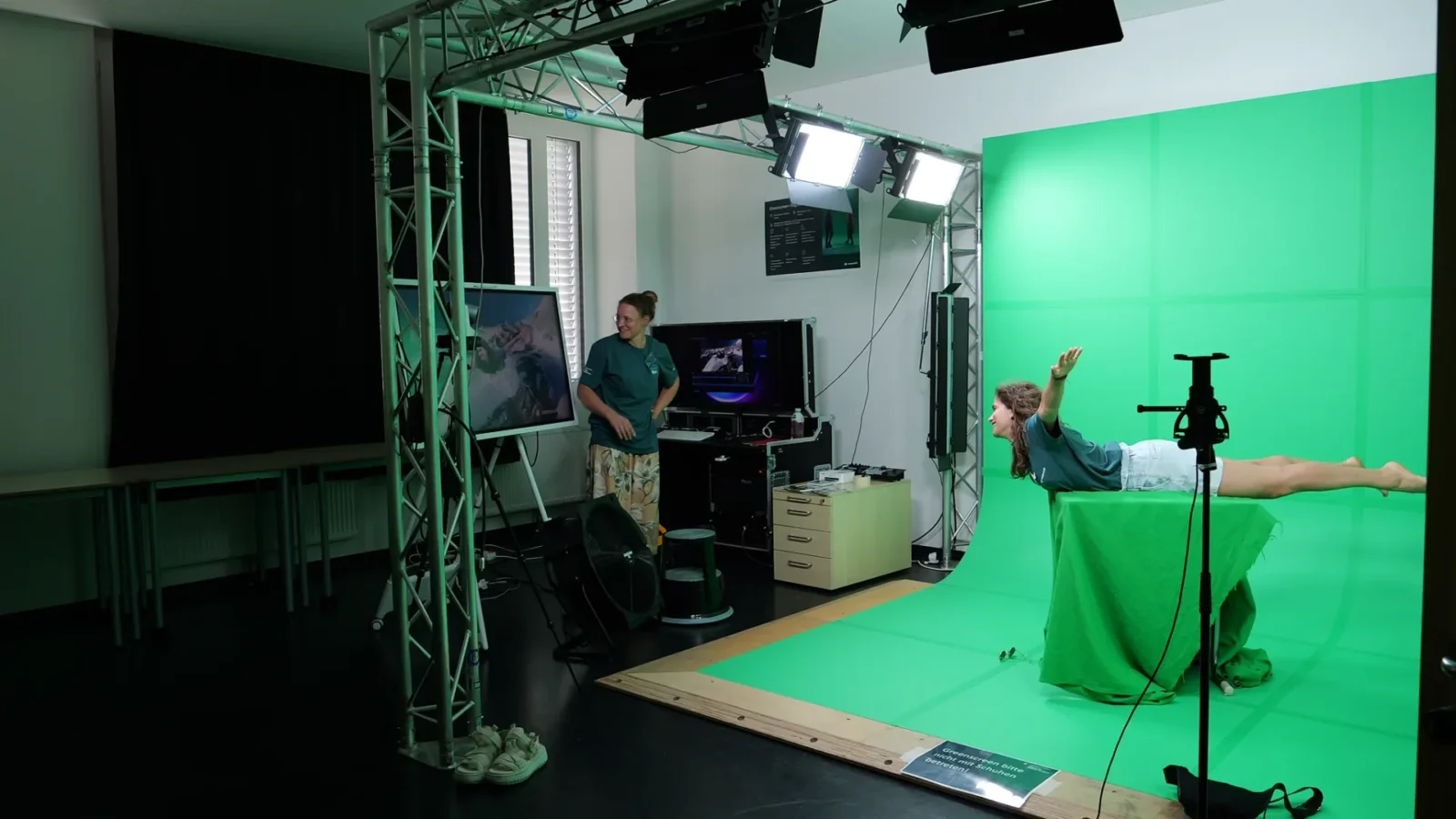 Greenscreen-Filmstudio: Person posiert in Flugpose auf einem grün verhüllten Tisch vor der Greenscreen-Wand