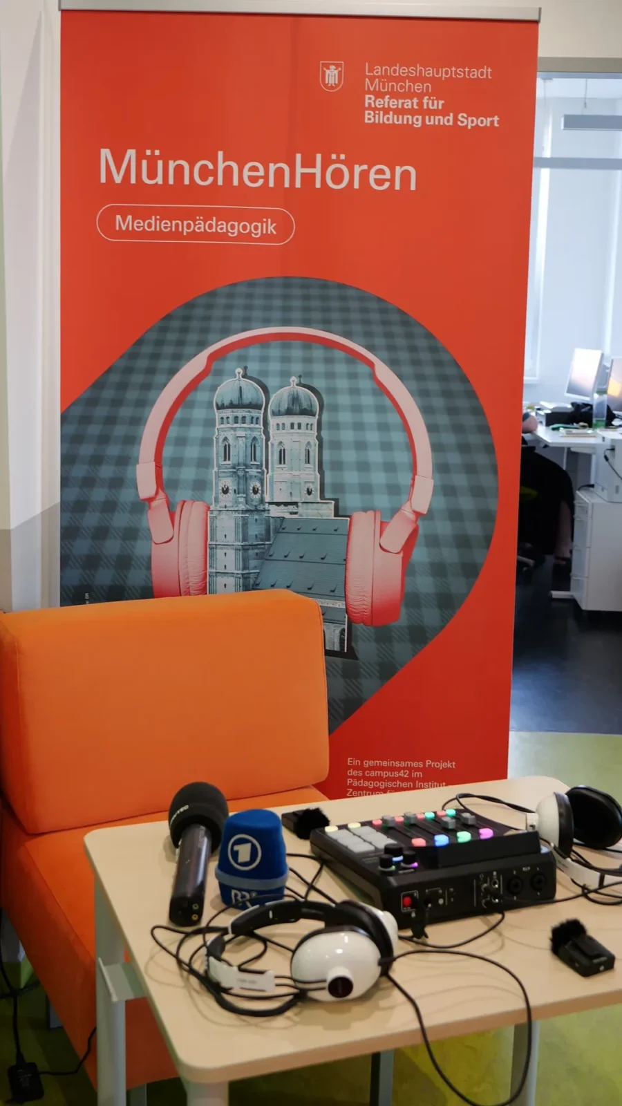 Podcast-Studio mit Mikrofonen, Mischpult und Kopfhörern vor dem Rollup „MünchenHören – Medienpädagogik"