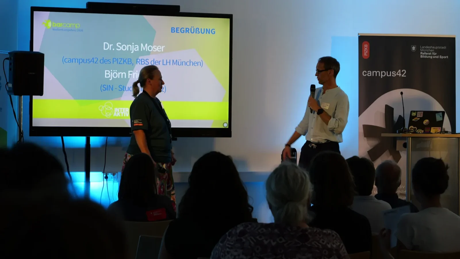 Begrüßung beim Barcamp Medienkompetenz 2026 vor der Titelfolie und dem campus42-Rollup